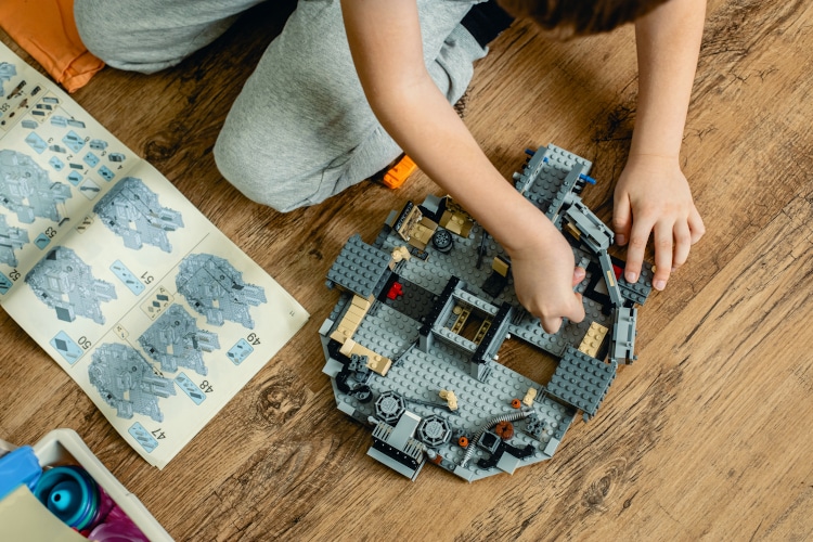 A teenage boy builds a Lego set of the Millennium Falcon at home in the children's room according to the instructions.